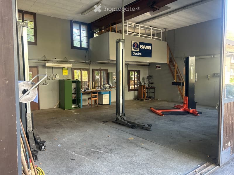 Garage with concrete floor, large windows, work area with tools, cabinets, and a chair.