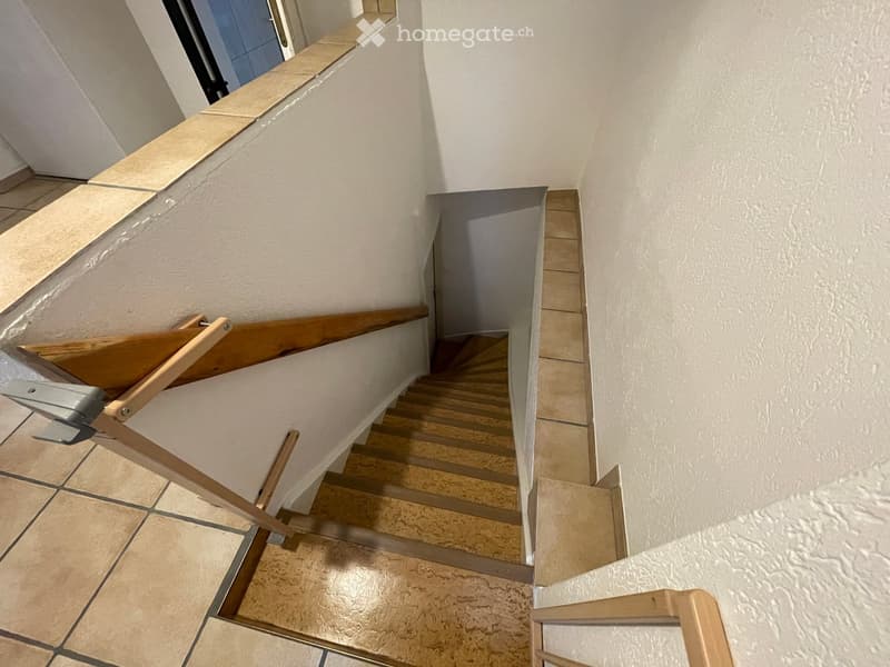 Interior shot of a wooden staircase with tiled floors leading up to a raised floor.