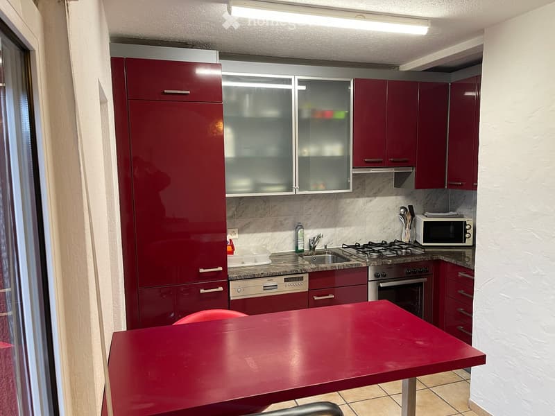 Red kitchen with marble counter top, oven, stove, microwave, dishwasher, cabinets and a red dining table