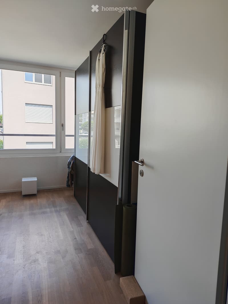 Empty hallway with wooden flooring, white walls, large window, and a sliding door leading to another room.