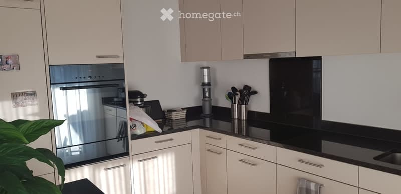 Modern kitchen with white cabinets, black countertop, stainless steel oven, coffee maker, and various kitchen utensils on the counter.