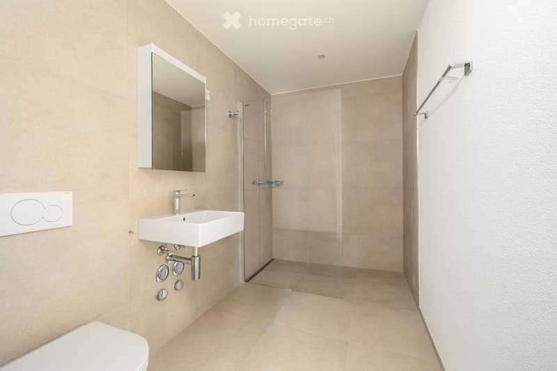 Modern bathroom with beige tiles, a white toilet, a wall-mounted sink with a chrome faucet, a large mirror, and a glass-enclosed shower area.