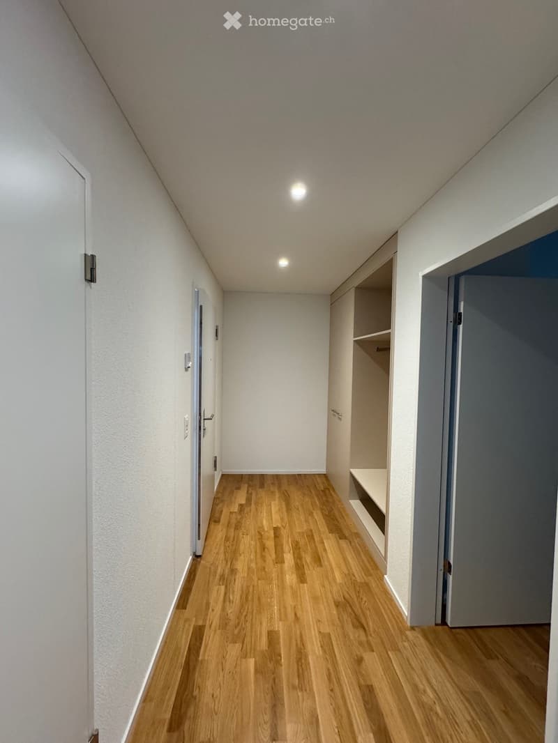 Empty hallway with wooden flooring, white walls, and recessed lighting. Features built-in shelving on one side and doors leading to other rooms.