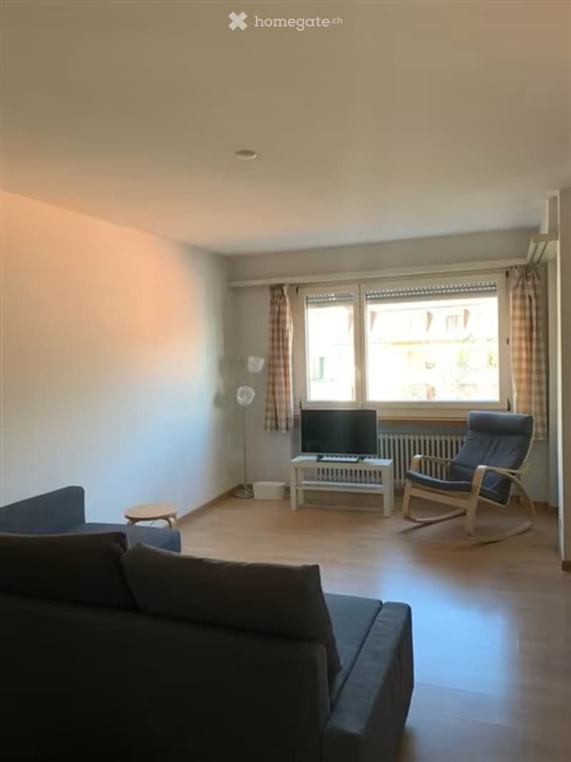 Modern living room with a dark blue sectional sofa, a white coffee table, a television on a stand, a rocking chair, and a floor lamp near the window.