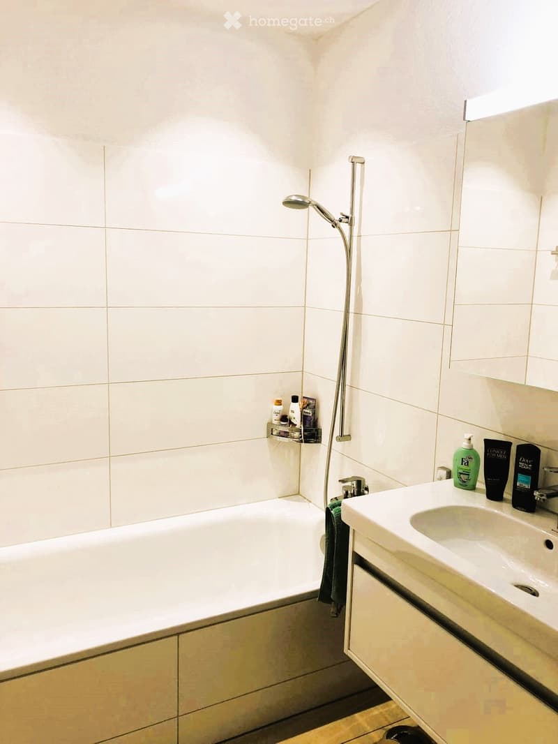 Modern bathroom with a white bathtub, a sink with a faucet, a showerhead, a mirror, and a towel on the edge of the bathtub.