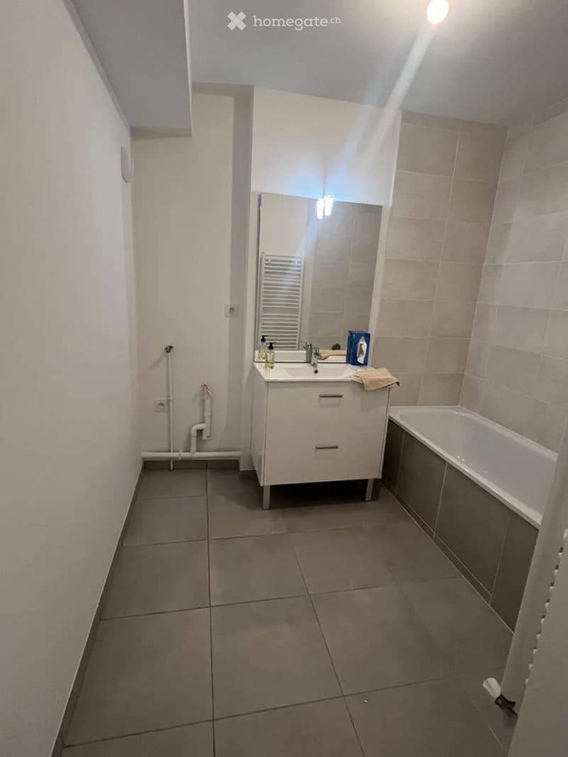 Modern bathroom with tiled walls and floor, white sink with mirror, bathtub, and towel on the counter.