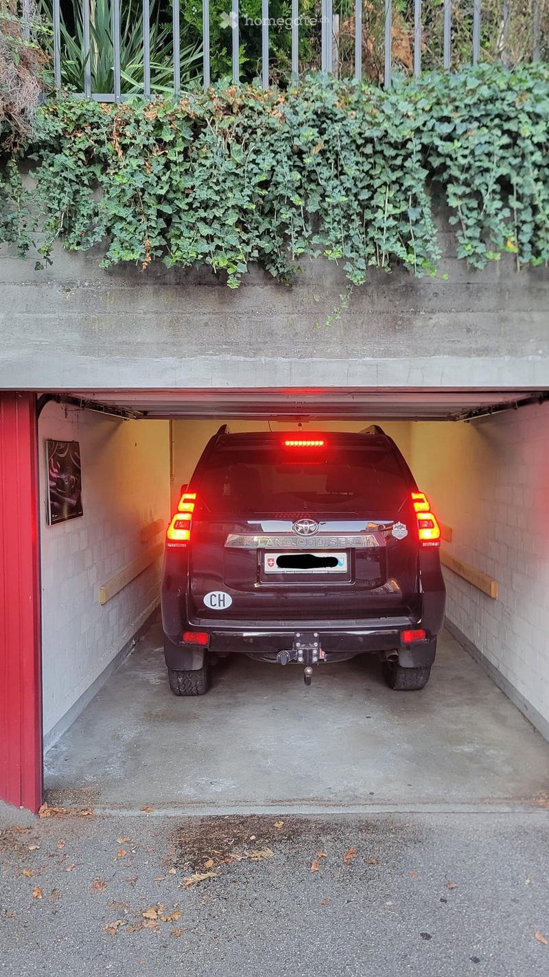 Underground garage with a parked red Land Cruiser SUV, surrounded by concrete walls and a metal gate.
