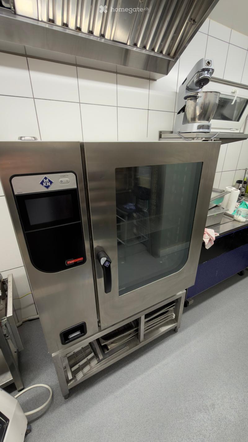 Commercial kitchen with stainless steel appliances, including an oven and a mixer, on a tiled countertop.