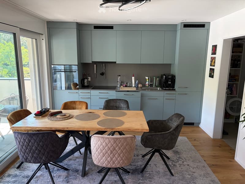 Modern kitchen and dining area with light blue cabinets, a wooden dining table with four chairs, and various kitchen appliances.