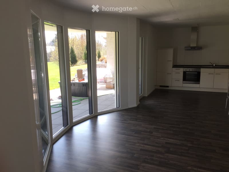 Bright, open-plan room with dark wooden flooring, large sliding glass doors leading to a patio, and a modern kitchen area with white cabinets and an oven.