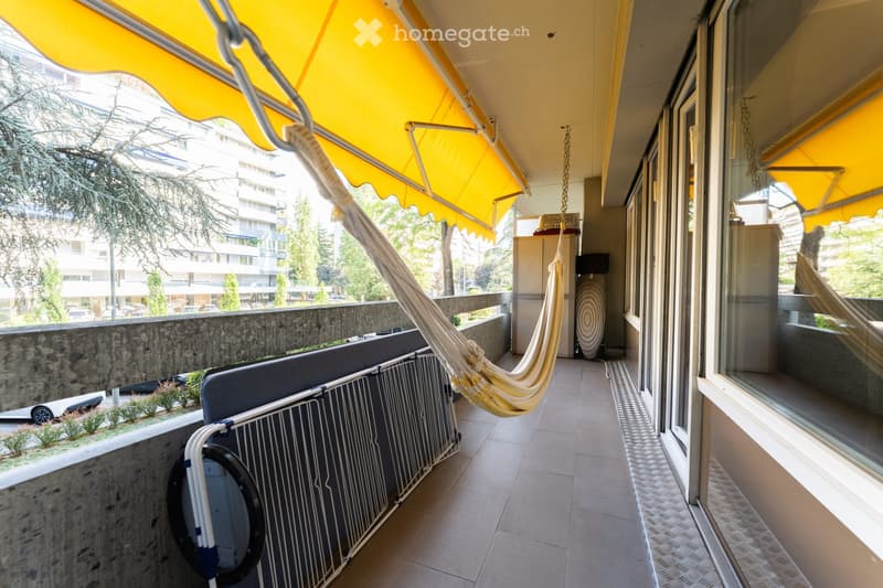Balcony with tiled floor, yellow awning, hammock, metal railing, and outdoor furniture.
