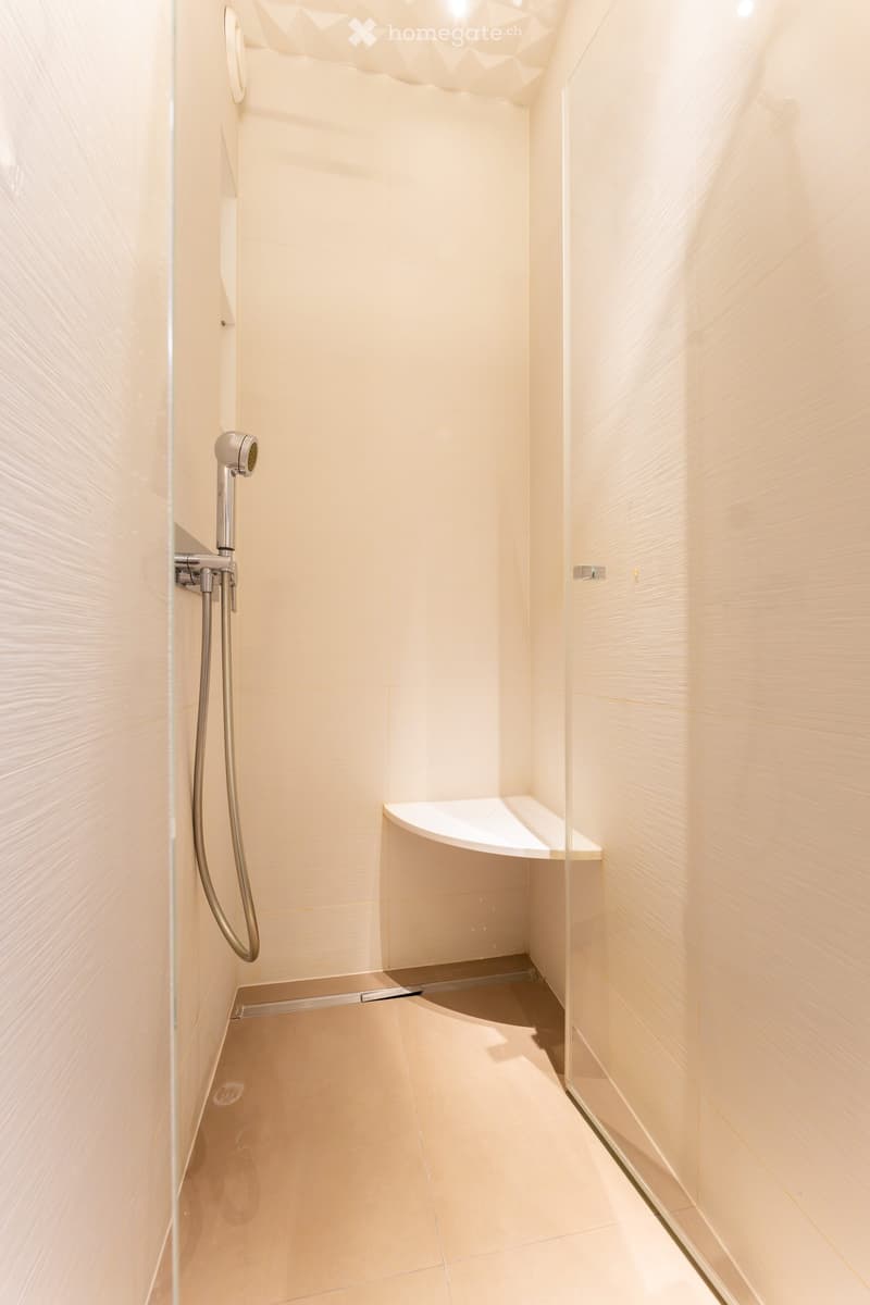 Modern shower area with light-colored tiles, a glass partition, a built-in shelf, and a sleek showerhead.