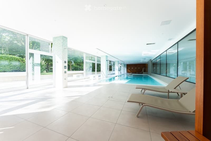 Spa area with indoor swimming pool, lounge chairs, large windows, and a view of greenery outside.