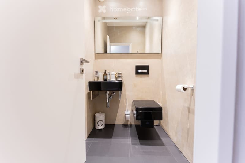 Modern bathroom with a black sink, toilet, large mirror, and beige walls.
