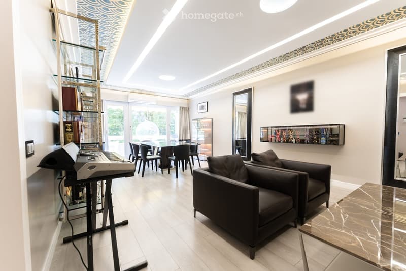 Modern, open-concept living and dining area with a sleek black sofa, dining table with chairs, a piano, and decorative mirrors. The space features a high ceiling with recessed lighting and a decorative border.