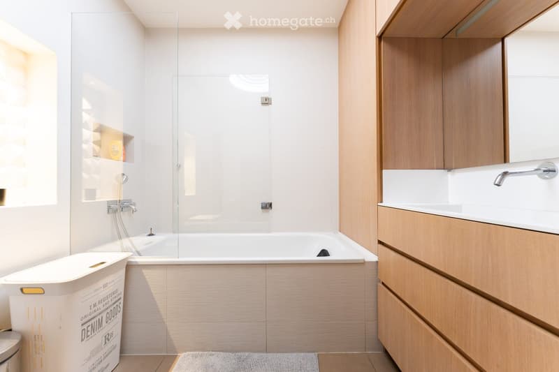 Modern bathroom with a white bathtub, glass shower enclosure, wooden vanity with sink, and a large mirror above the sink.