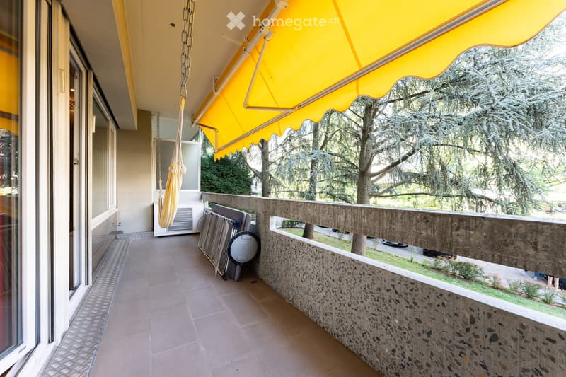 Balcony with yellow awning, tiled floor, stone railing, and outdoor furniture stored against the wall.