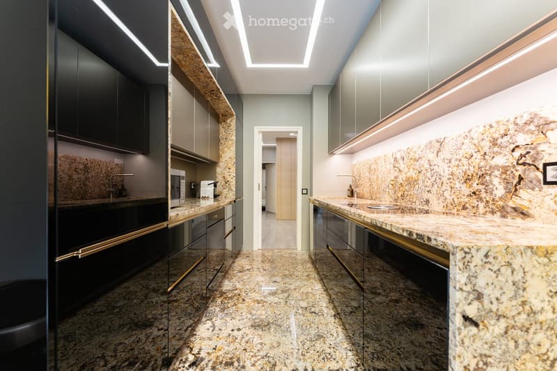 Modern kitchen with granite countertops, sleek black and grey cabinets, built-in appliances, and ambient lighting.
