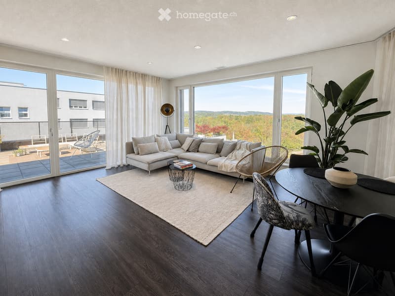 Modern living room with large windows, a sectional sofa, a coffee table, dining area with chairs and table, and a large plant. The room features wooden flooring and a neutral color palette.