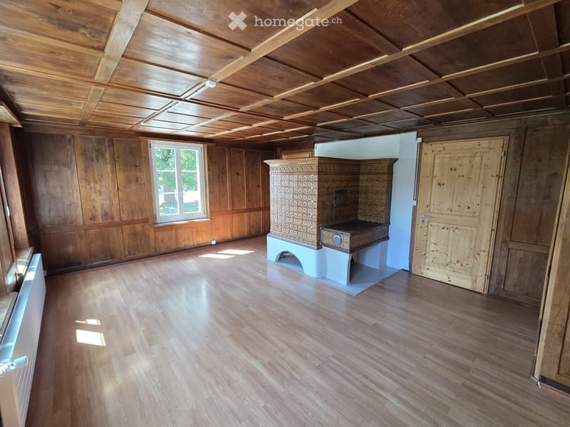 Empty room with wooden walls, wooden ceiling, wooden floor, and a fireplace with a decorative surround. There is a window on one wall and a door on another.