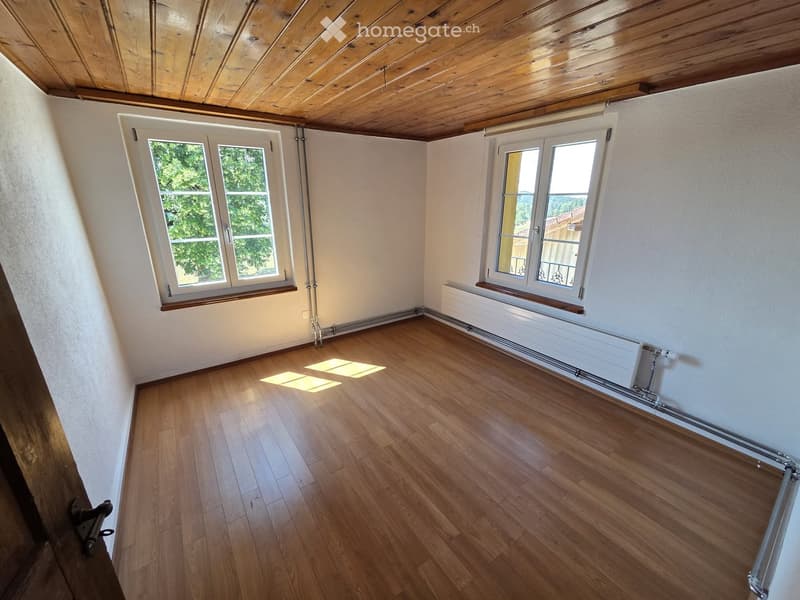 Empty room with wooden flooring, white walls, and large windows with wooden frames. The ceiling is wooden, and there is a radiator along one wall.