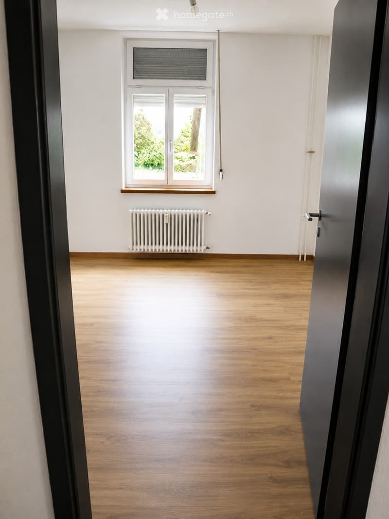 Empty room with wooden flooring, white walls, a window with blinds, and a radiator below the window.