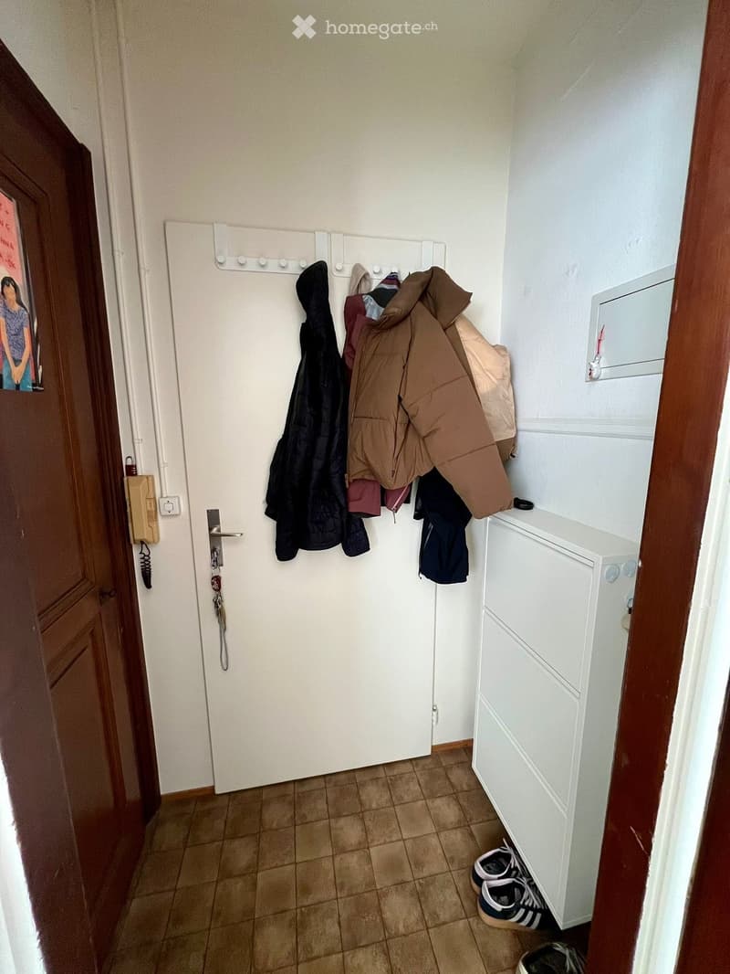 Entryway with tile flooring, white walls, white door, coat rack with hanging coats, white storage cabinet, shoes on the floor