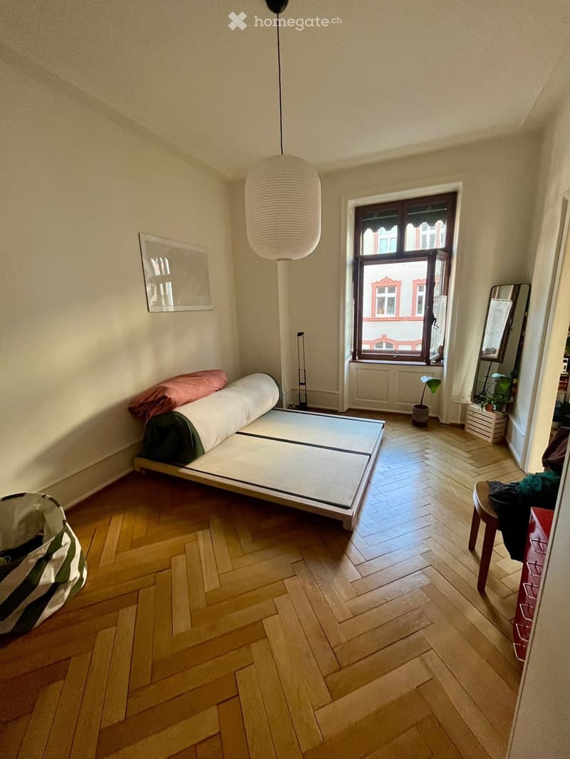 Minimalist bedroom with tatami mat bed, wooden floor, large window, hanging lamp, small stool, mirror, and potted plant.