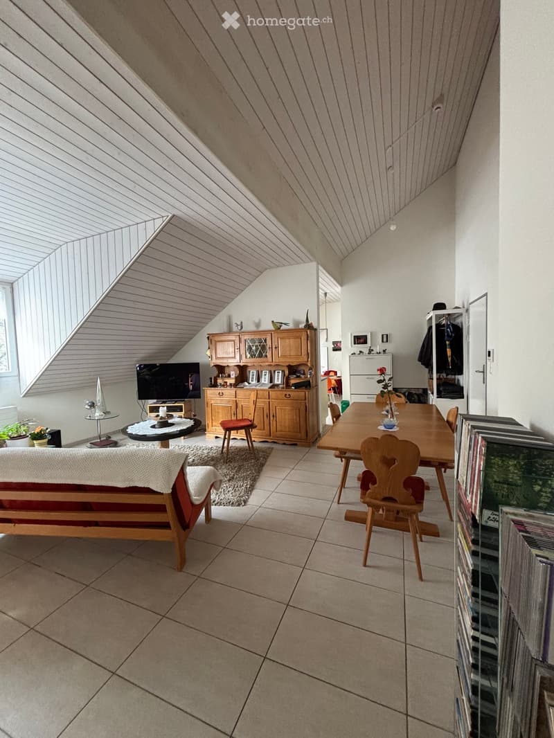 A room with a wooden dining table, chairs, a wooden cabinet, a TV, a couch, a rug, and a shelf with books.