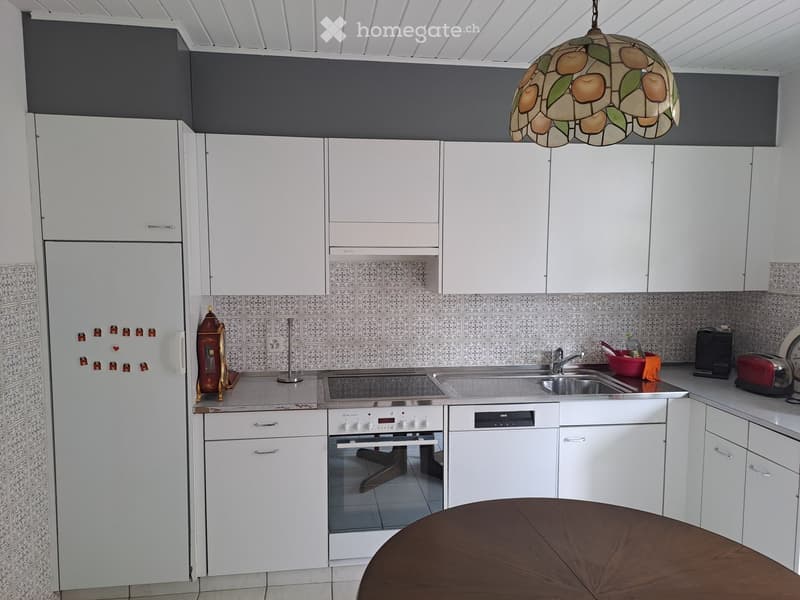 Modern kitchen with white cabinets, stainless steel appliances, and a round wooden table in the foreground.