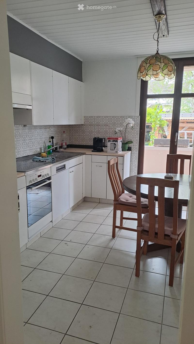 Modern kitchen with white cabinets, tiled backsplash, and a dining area with a round table and chairs. Features an oven, dishwasher, sink, and coffee maker.