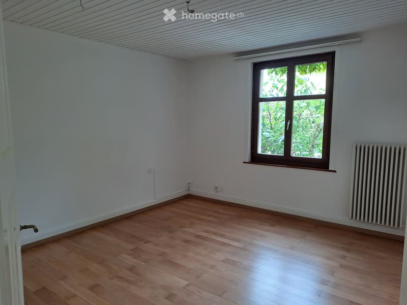 Empty room with light wooden flooring, white walls, a window with brown frame, radiator, and electrical outlets.