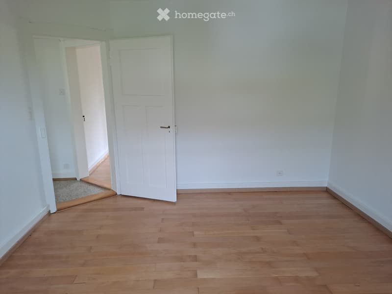Empty room with light wooden flooring and white walls, featuring an open doorway leading to another room.