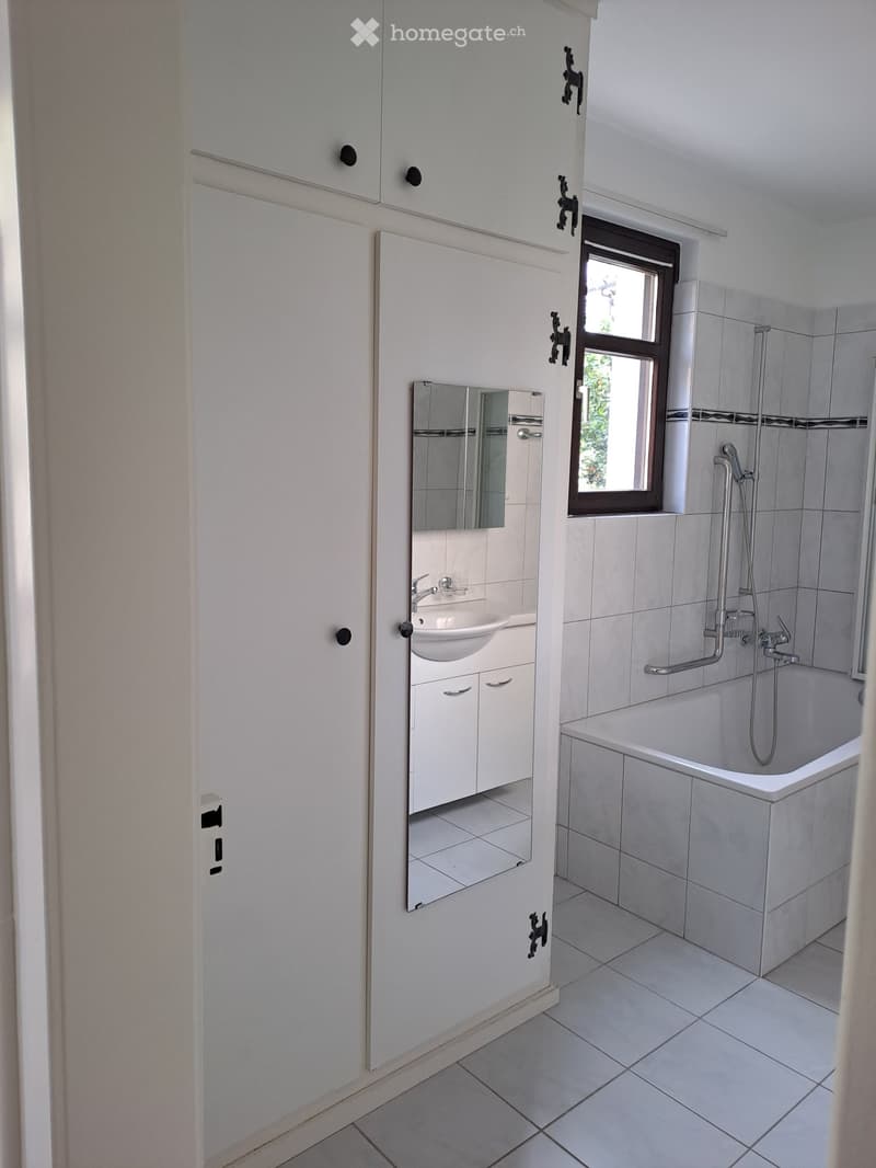 Modern bathroom with white tiles, a bathtub, a sink with a mirror, and a window providing natural light.