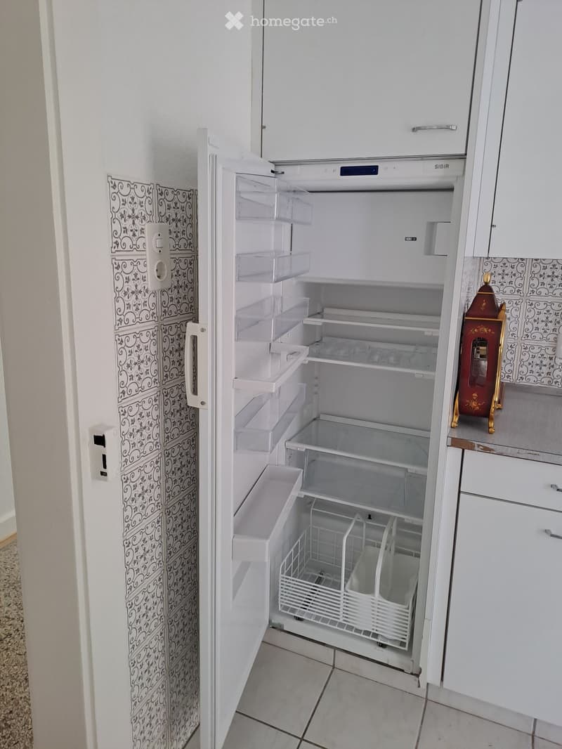 Open refrigerator with multiple shelves and drawers, white cabinets, and decorative wall tiles.