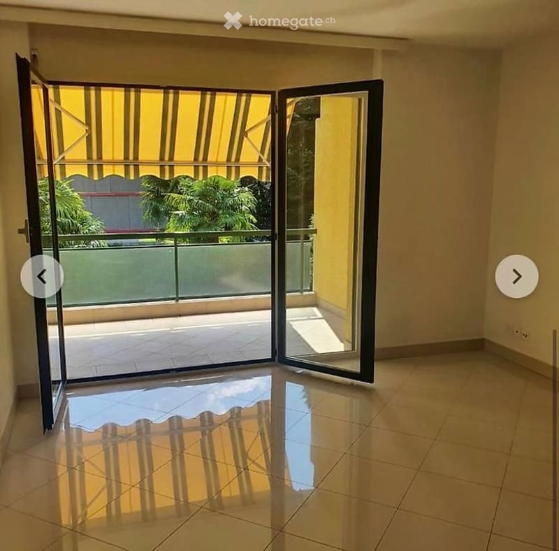 Empty room with tiled floor, large sliding glass doors leading to a balcony with a yellow awning and outdoor view.