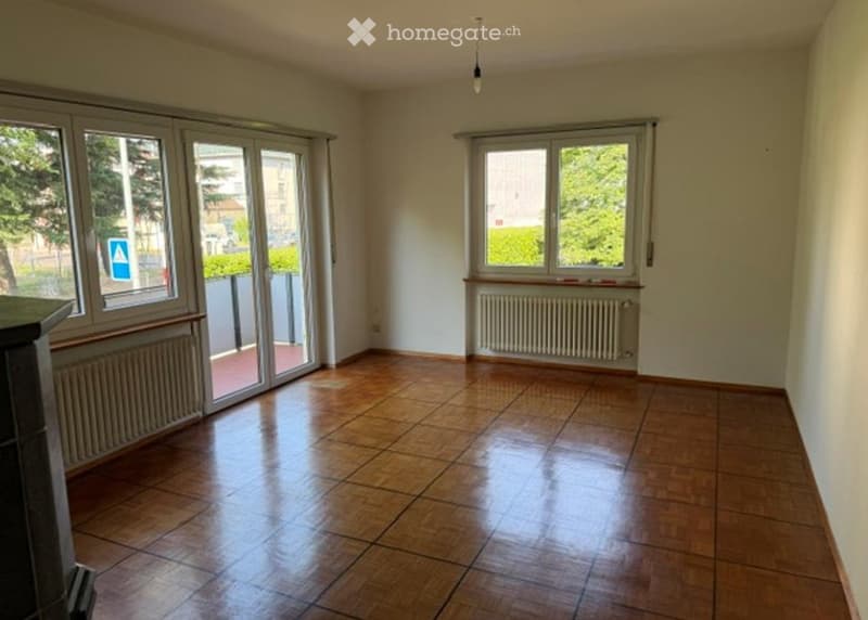 Empty room with wooden flooring, large windows, and sliding glass doors leading to a balcony.