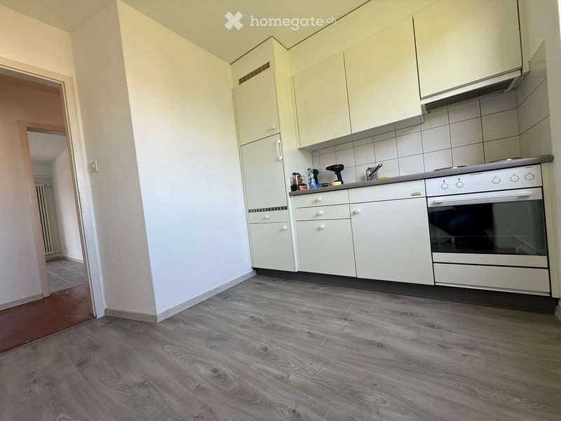 Modern kitchen with white cabinets, grey tiled backsplash, and a stainless steel oven. Wooden flooring and a grey countertop.