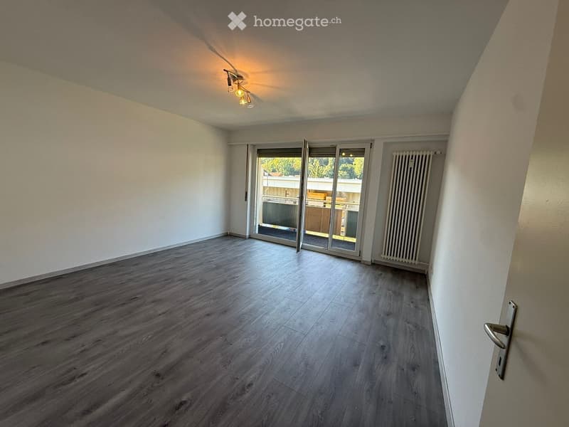 Empty room with wooden flooring, white walls, and a sliding glass door leading to a balcony area.