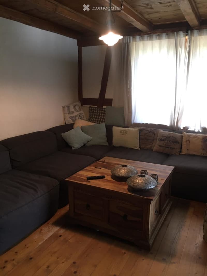 L-shaped sofa, pillows, coffee table, remote control, light hanging from ceiling, curtain