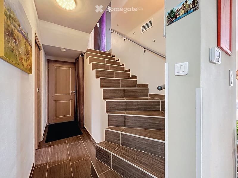 Modern hallway with wooden tiled flooring, staircase with wooden steps and metal railing, white walls, and framed artwork.
