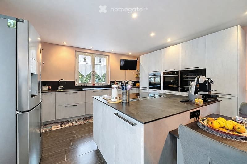 Modern kitchen with white cabinets, granite countertop, stainless steel appliances, and a breakfast area with a chair and table.