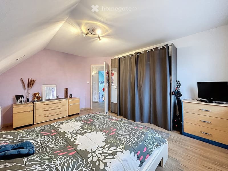 Cozy attic bedroom with slanted ceilings, wooden floors, and modern furnishings including a bed, dressers, a mirror, and an exercise bike.