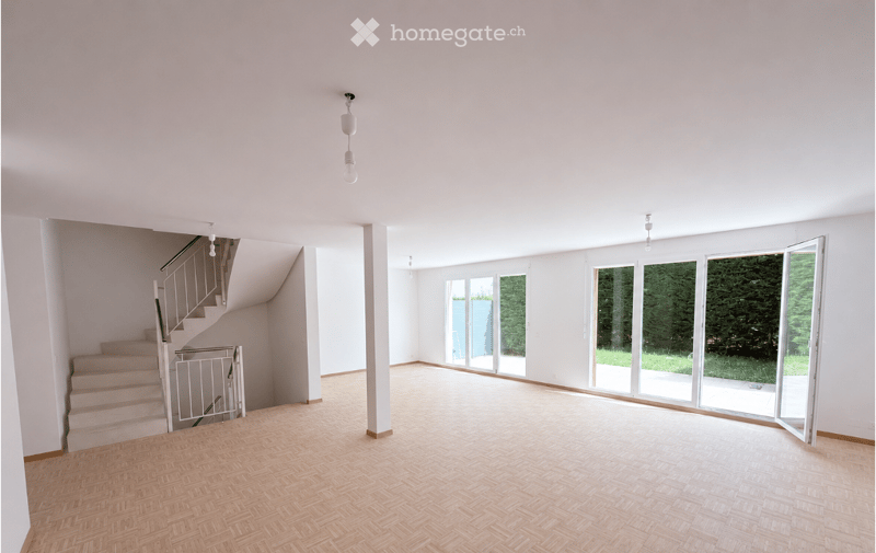 Completely empty room with wooden herringbone flooring, white walls, and large glass doors leading to an outdoor area.