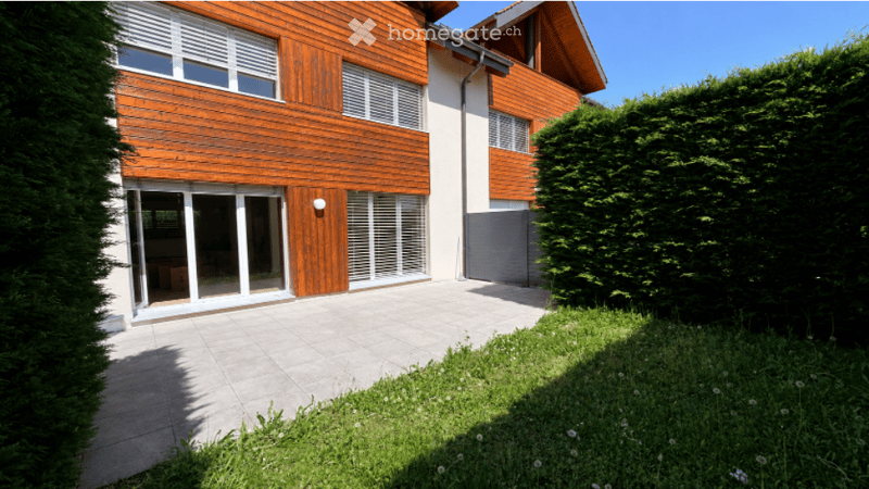 Modern two-story house with wooden siding, large windows, and a spacious patio area.