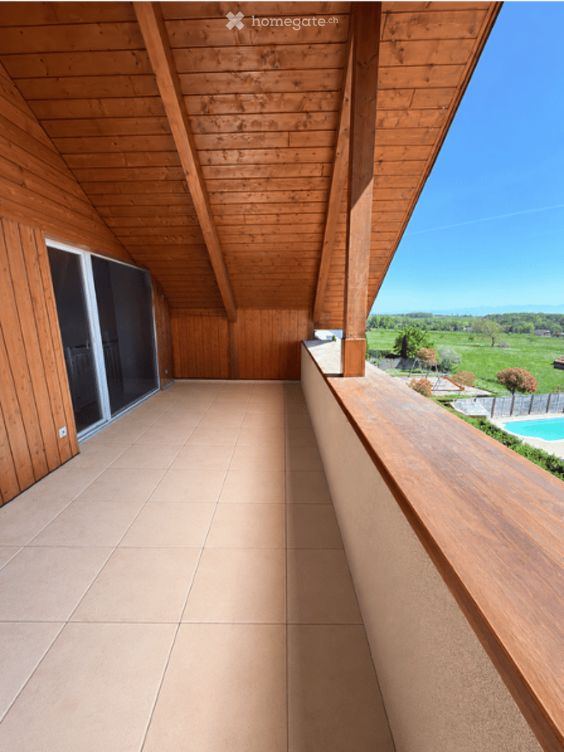 Wooden balcony with tiled floor, large windows, and a view of a green field and swimming pool.