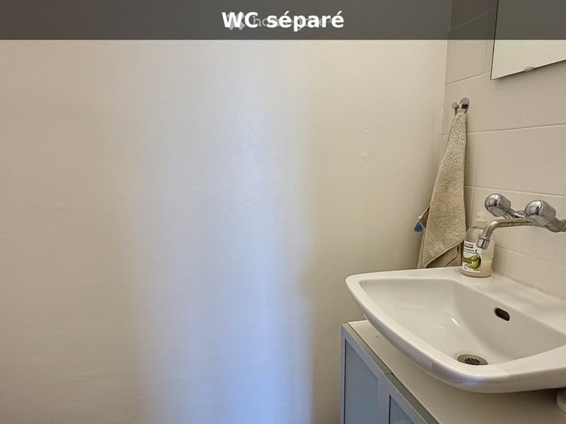 A small bathroom with a white sink, chrome faucet, a mirror above it, and a towel hanging on the wall.