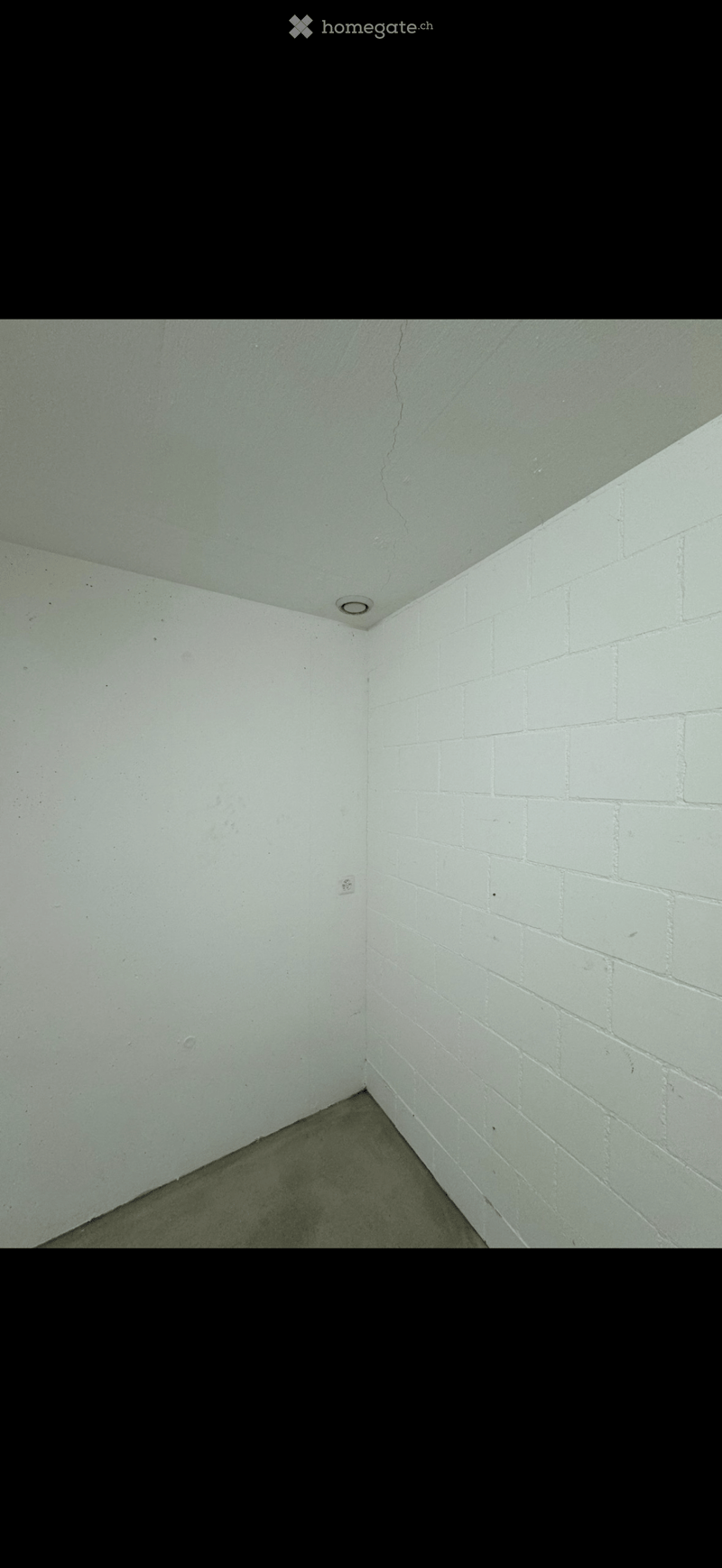 Empty room with white brick walls, concrete floor, and a single ceiling light fixture.