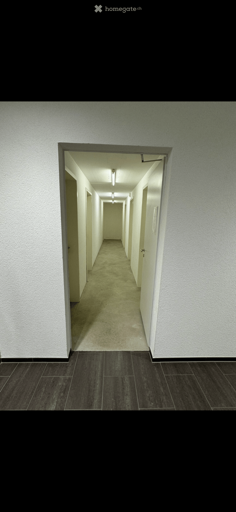 Empty hallway with white walls, dark tiled floor, and multiple doors on both sides.