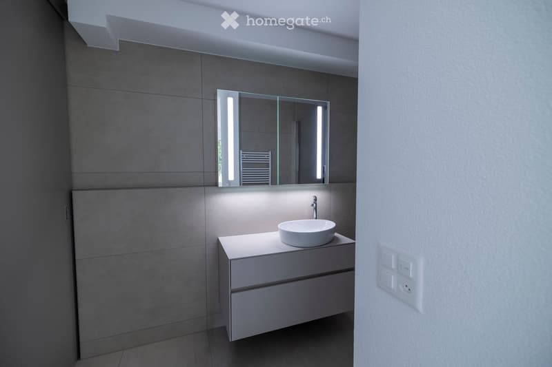 Modern bathroom with a white sink, sleek mirror with built-in lighting, and a minimalist cabinet.